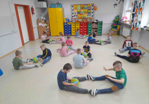 Dzieci siedzą na podłodze i turlają do siebie piłki